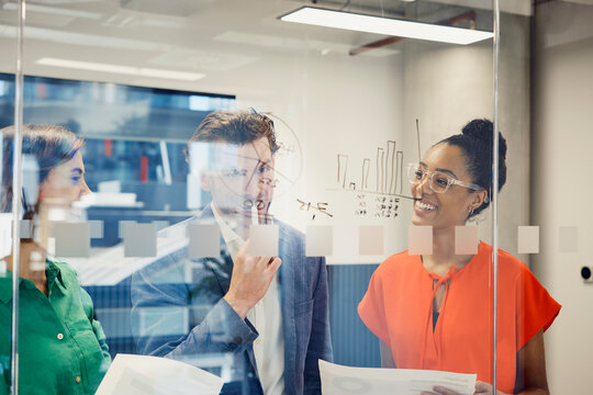 Smiling multiracial business colleagues discussing in meeting behind glass wall