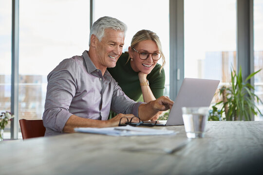 Smiling mature couple using laptop on table at home
