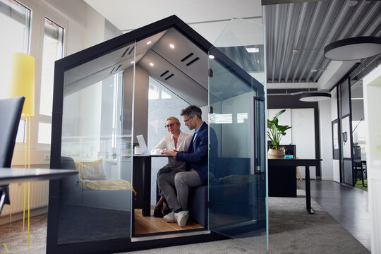 Business colleagues working on laptop sitting in office cubicle