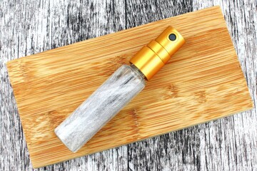 Small, spray perfume bottle on light brown bamboo cutting board