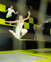Young girl acrobatic athlete jumping and exercising on trampoline indoors, modern hobby and fitness...