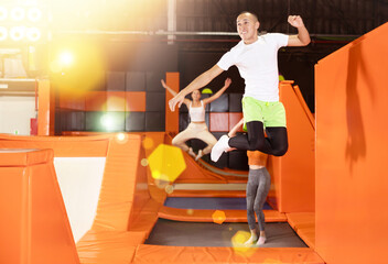 Energetic young man exuding joy while leaping at trampoline park, showcasing carefree fun of indoor...