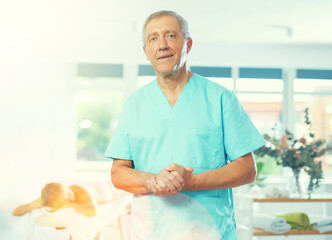 Portrait of male massage therapist standing at bright massage room of SPA center