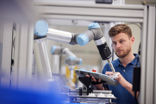 Engineer testing robotic arm using equipment in industry