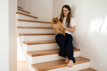 Young woman bonding with her Pomeranian dog on stairs at home