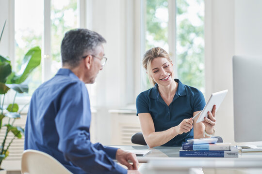 Smiling female doctor discussing over tablet PC with patient in medical practice