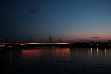 Orange-lit bridge over the Sava River in Belgrade at sunset, reflecting beautifully on calm water...