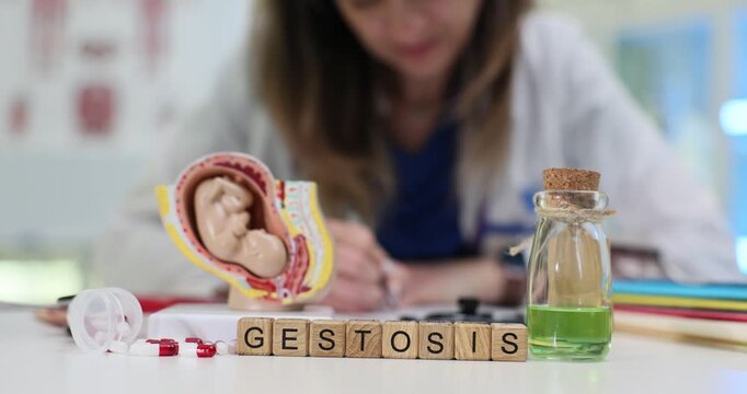 Gestosis word made from wooden cubes symbolizes pregnancy related risks shown on uterus model. Behind blocks doctor takes notes creating medical scene