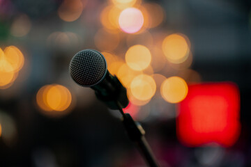 Microphone on stand with glowing bokeh lights in background, symbolizing live concert, public...