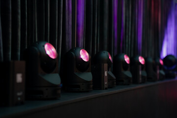 Row of moving head LED stage lights emitting pink glow in front of dark curtains, professional...