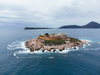 Aerial shot of rocky islet with red roofed building in Montenegro surrounded by turquoise Adriatic...