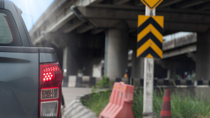 Traffic view showing a car tail light. A yellow black hazard sign and road barriers under an...