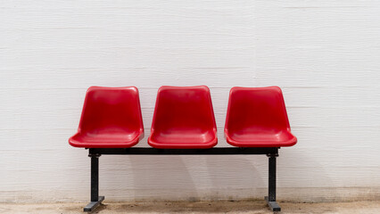 Three vibrant red plastic chairs against a white textured wall, forming an empty waiting area....