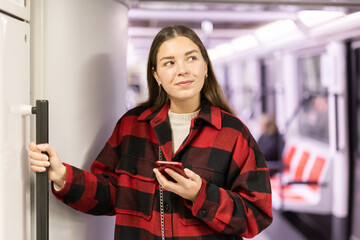 In subway car, girl with phone standing in carriage, go to work, get bored on way and chatting on...