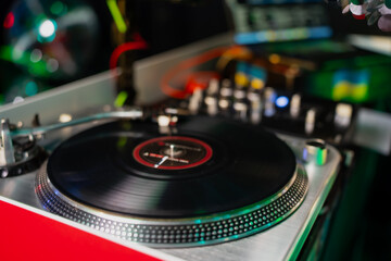 DJ turntable with spinning vinyl record in colorful club lighting, professional audio setup with...