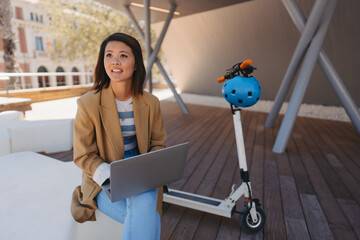 Young Asian female student using a laptop in front of the university
