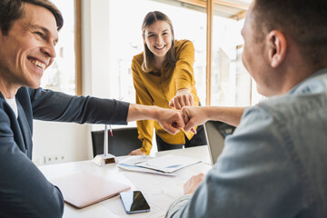 Happy business team touching fists in office