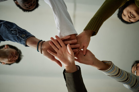 Diverse group of teenagers joining hands in teamwork gesture during counseling session, multiethnic boys and girls collaborating and supporting each other, viewed from below