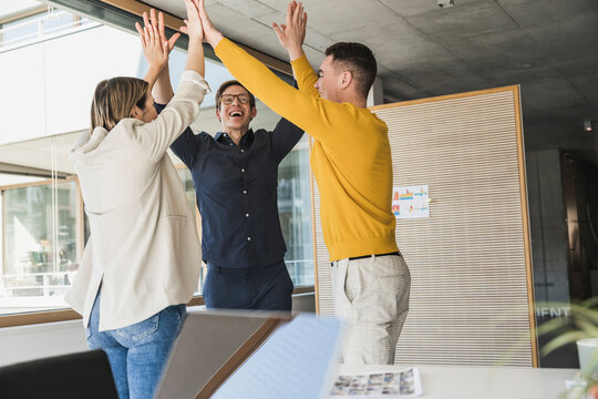 Happy business people standing together with raised arms in office