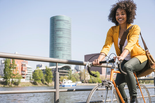Happy businesswoman riding bicycle by River Main on sunny day