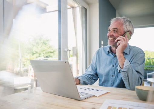 Smiling freelancer talking on smart phone at home