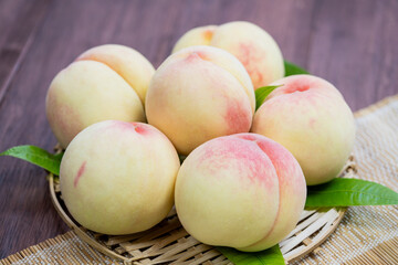 White Peaches with leaves on the wooden table, Fresh White Peach on wooden basket in wooden Background.