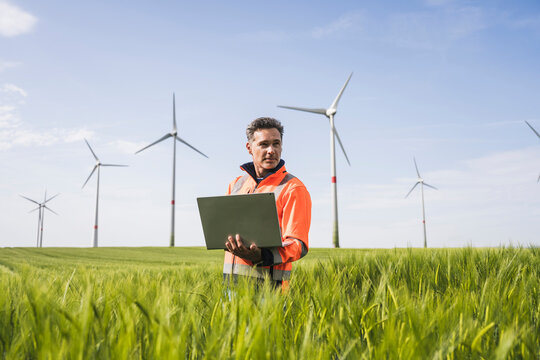 Engineer with laptop standing amidst wheat crops on field
