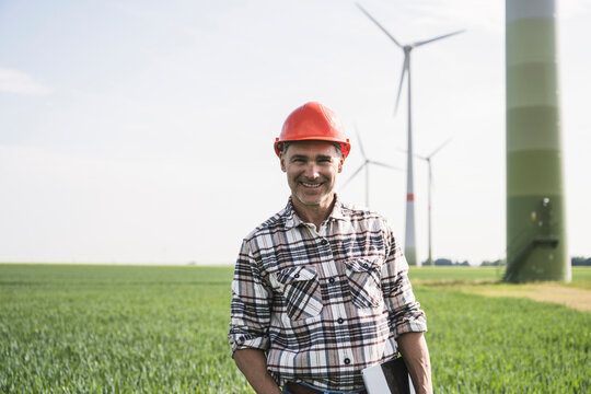 Smiling engineer wearing hardhat standing with tablet PC at field