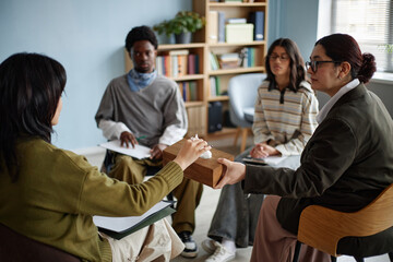 Diverse group of teenagers participating in counseling session with adult woman facilitator,...