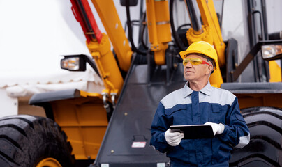 Industrial engineer uses computer tablet to manage production. Adult man in uniform and yellow...