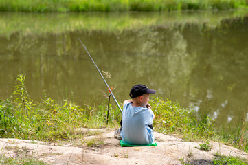 Boy fishing alone on pond shore in summer landscape
