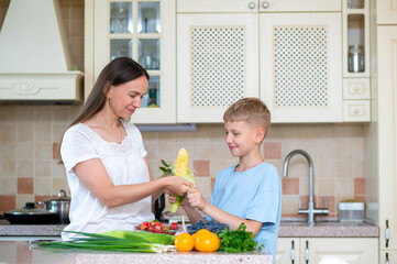 Mother and son preparing corn and vegetables in home kitchen