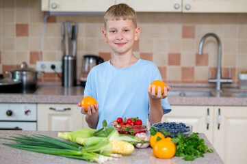 Blond teenage boy holding yellow tomatoes in bright kitchen with fresh vegetables and berries