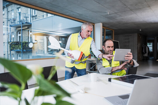 Elderly engineer with wind turbine rotor explaining colleague at office