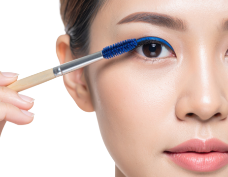 A close-up of a woman applying vibrant blue mascara to her eyelashes against a black background.