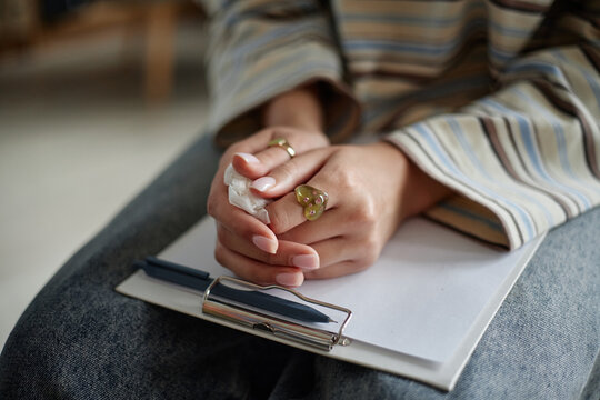 Teenager girl sitting during counseling session holding tissue in hands resting on clipboard with pen showing emotional support and vulnerability