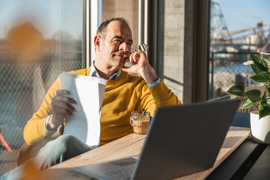 Thoughtful mature businessman with document sitting in office - Powered by Adobe