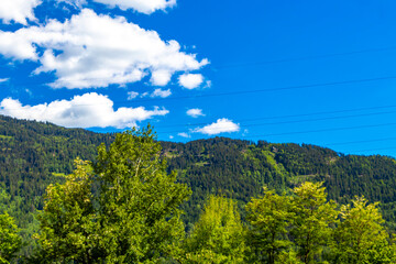 Alpine mountain landscape panorama green fields forest blue sky and clouds.