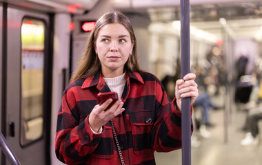 During trip to work in subway car, passenger girl with phone stand and holding on to handrail,...