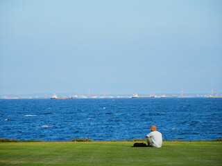 夏の新浦安総合公園の芝生で休憩する男性の姿と東京湾の風景