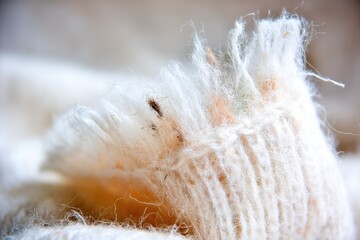 Close-up of a torn, frayed edge of a knitted cream-colored garment