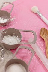 Pastry chef tools, cooking process, measuring spoons, brush, rolling pin, wooden spoon, pink silicone dough mat, vertical image