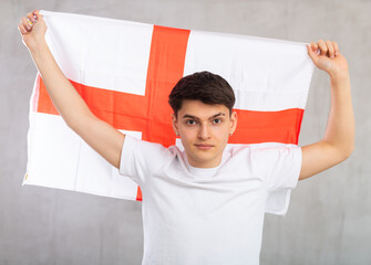 Young focused guy posing with big flag of England in his hands in studio....