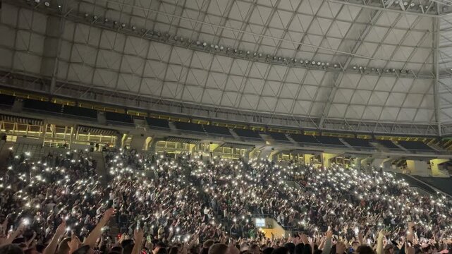 People lift hand up hold cell phone flashlight. Fan crowd wave flashlights. Epic live music concert atmosphere.