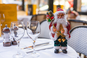 A festive table setting with two wine glasses and a decorative Santa Claus figurine. The scene captures the spirit of Christmas and New Year celebrations.