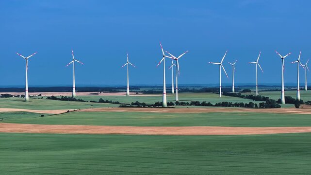 Aerial view of wind turbines standing tall in a patchwork of green and brown fields under a clear blue sky, Brussow, Brandenburg, Germany.