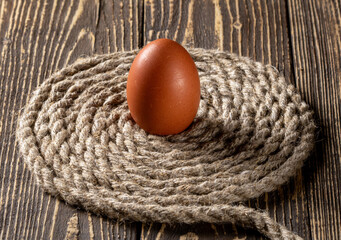 A fresh chicken egg resting on a textured jute rope background