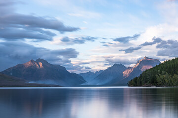 A serene landscape featuring a calm lake reflecting the surrounding mountains and sky, creating a peaceful and scenic view.
