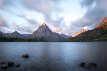 A scenic view of a lake surrounded by mountains, with the sun illuminating the peaks and creating a serene atmosphere.