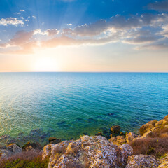 stony coast of the sea bay under a blue cloudy sky at the sunset